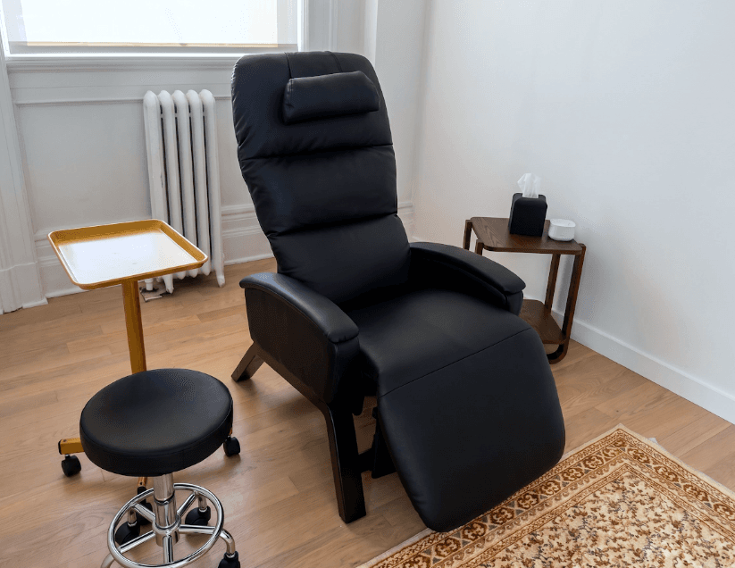 Black zero-gravity reclining chair with a wooden stool by a window