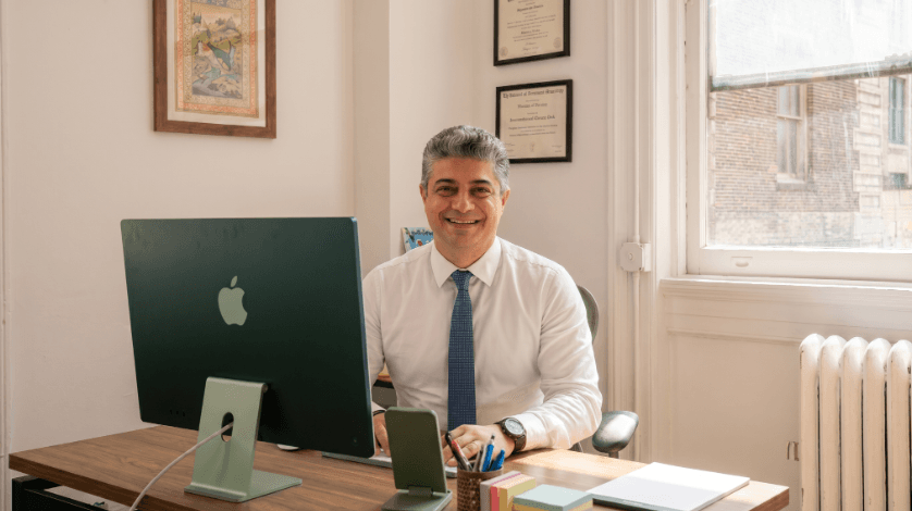 Dr. Omidvari smiling at his desk in front of a green iMac